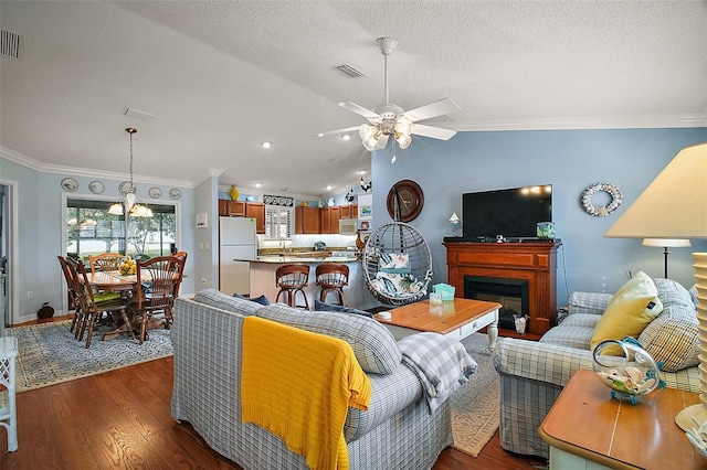 living area featuring visible vents, vaulted ceiling, wood finished floors, and ornamental molding