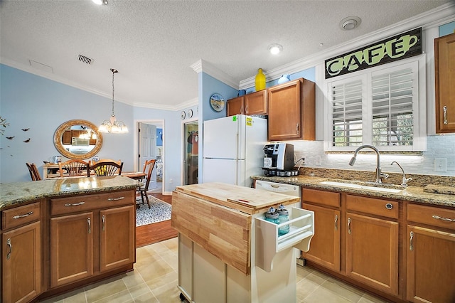 kitchen with white appliances, visible vents, brown cabinetry, light stone counters, and a sink