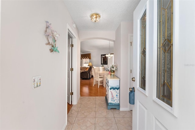 1202 San Bernardo Rd, The Villages, FL 32162 - hall featuring light tile patterned floors, baseboards, arched walkways, an inviting chandelier, and a textured ceiling