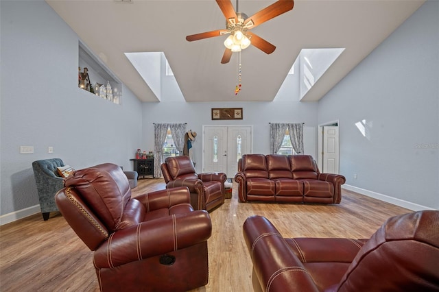 living room with high vaulted ceiling, a skylight, light wood-style flooring, and baseboards