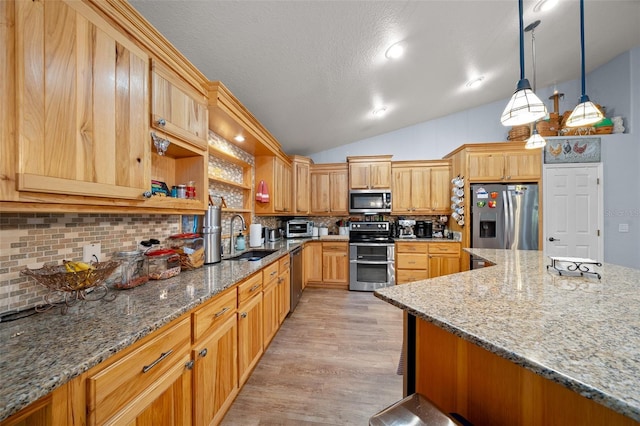 kitchen with vaulted ceiling, stainless steel appliances, light stone counters, and a sink