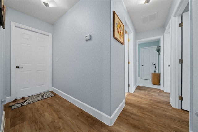 hallway with visible vents, a textured wall, baseboards, and wood finished floors