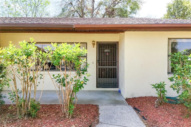 entrance to property with roof with shingles and stucco siding