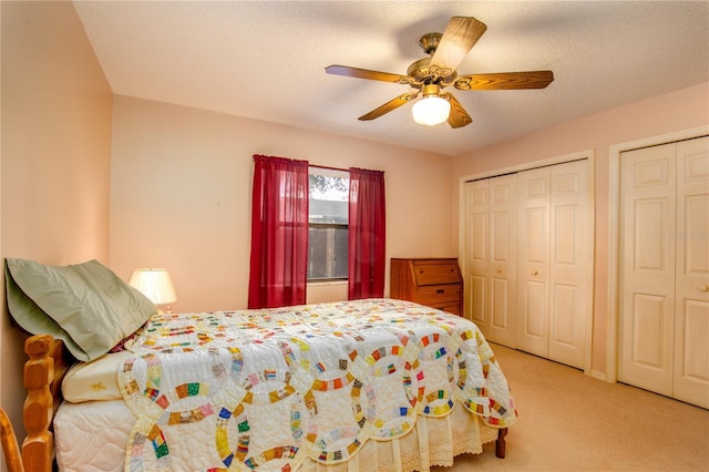 bedroom featuring a textured ceiling, multiple closets, a ceiling fan, and light colored carpet