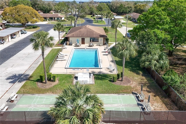 community pool with fence, a lawn, and shuffleboard