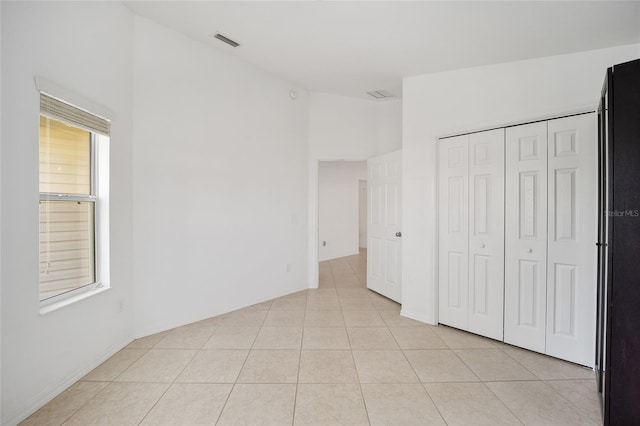 unfurnished bedroom with light tile patterned floors, high vaulted ceiling, visible vents, a closet, and freestanding refrigerator