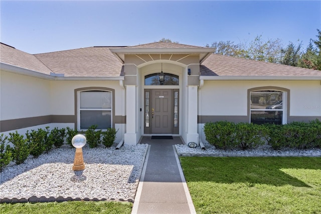 property entrance featuring a yard, a shingled roof, and stucco siding