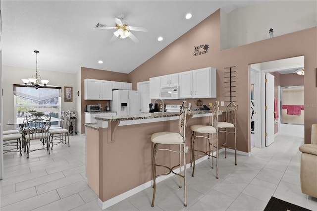 kitchen with a peninsula, white appliances, stone countertops, and a breakfast bar