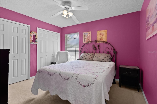 carpeted bedroom featuring a ceiling fan, a textured ceiling, baseboards, and two closets