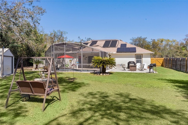 back of property with glass enclosure, a fenced backyard, solar panels, a yard, and a patio area