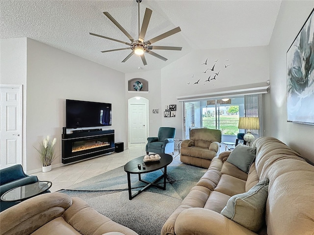 living room featuring light tile patterned floors, a ceiling fan, a glass covered fireplace, lofted ceiling, and a textured ceiling