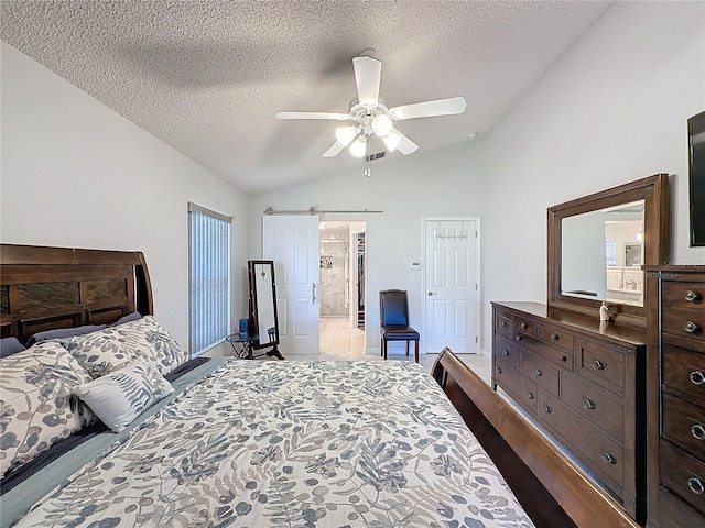 bedroom with vaulted ceiling, a textured ceiling, ensuite bath, and a barn door