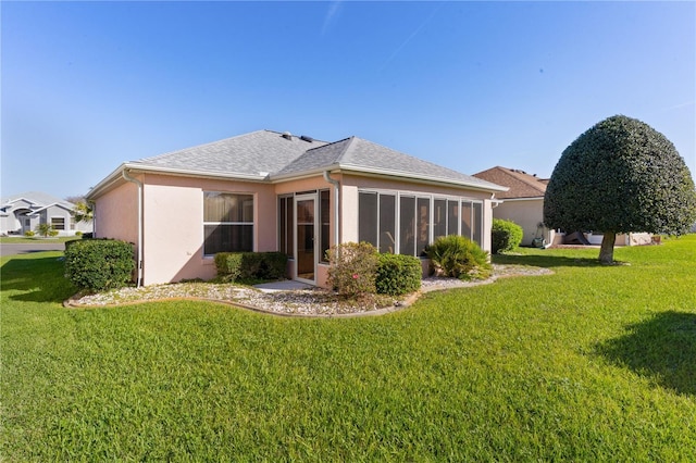 rear view of property with a yard, roof with shingles, a sunroom, and stucco siding