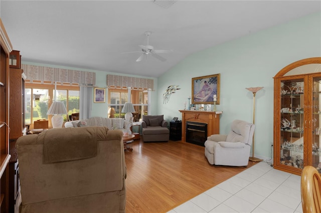 living area with visible vents, a ceiling fan, a glass covered fireplace, vaulted ceiling, and light wood-style floors