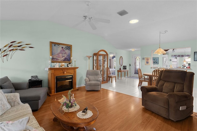 living room with lofted ceiling, light wood-style floors, visible vents, and a glass covered fireplace