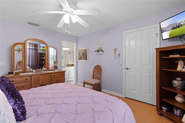 bedroom with a textured ceiling, visible vents, a ceiling fan, light wood-type flooring, and ensuite bath