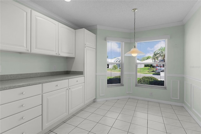 unfurnished dining area with a wainscoted wall, ornamental molding, and a textured ceiling