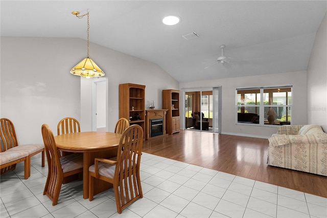 dining space featuring a ceiling fan, a glass covered fireplace, lofted ceiling, and light wood-style floors