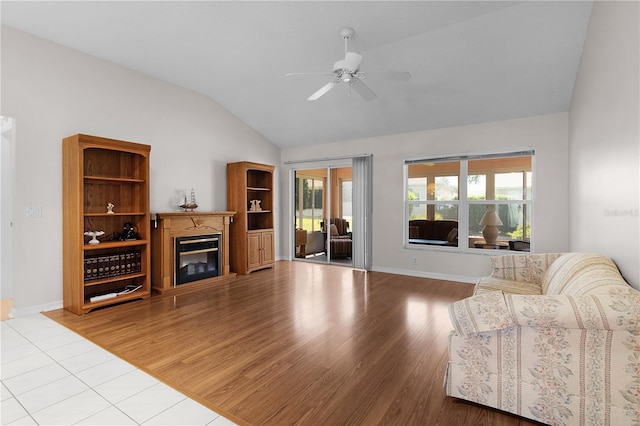 living area featuring ceiling fan, vaulted ceiling, wood finished floors, baseboards, and a glass covered fireplace