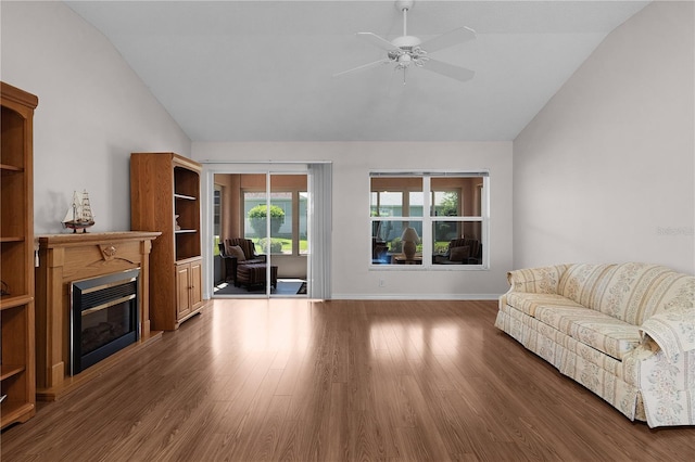 living area featuring a glass covered fireplace, wood finished floors, lofted ceiling, baseboards, and a ceiling fan