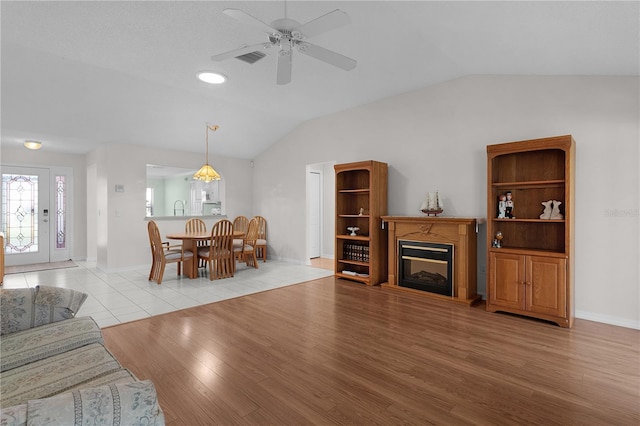 living room with a glass covered fireplace, lofted ceiling, light wood-style floors, baseboards, and a ceiling fan