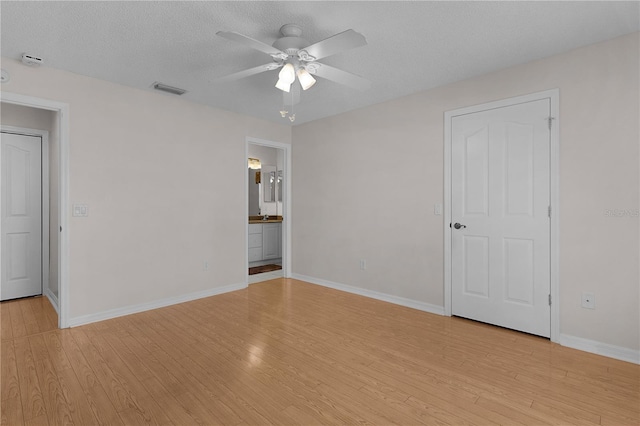 interior space featuring a textured ceiling, visible vents, baseboards, light wood finished floors, and ensuite bath