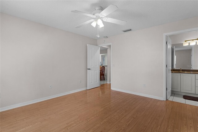 unfurnished bedroom with baseboards, light wood finished floors, a textured ceiling, and visible vents