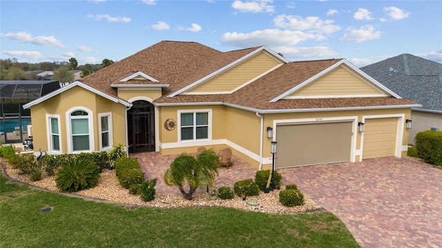 ranch-style house with stucco siding, an attached garage, a shingled roof, and decorative driveway