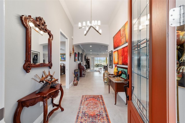 entrance foyer with ornamental molding, baseboards, arched walkways, and a chandelier