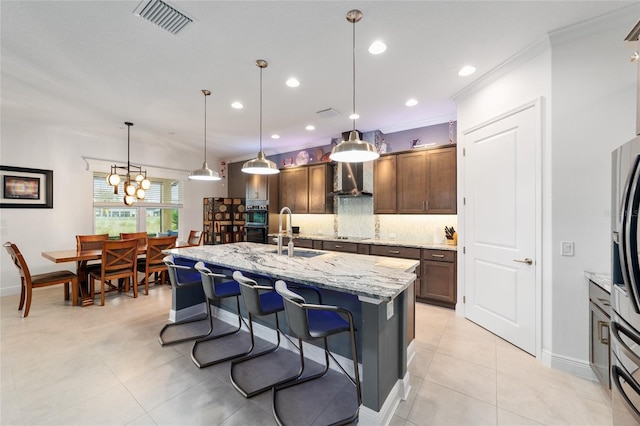 kitchen featuring visible vents, a sink, decorative backsplash, black appliances, and wall chimney range hood