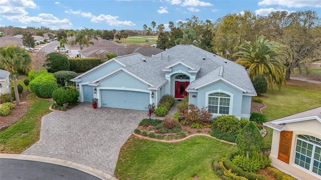 view of front of house with decorative driveway, roof with shingles, stucco siding, an attached garage, and a front lawn