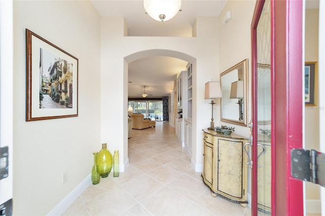 corridor featuring light tile patterned floors, baseboards, and arched walkways