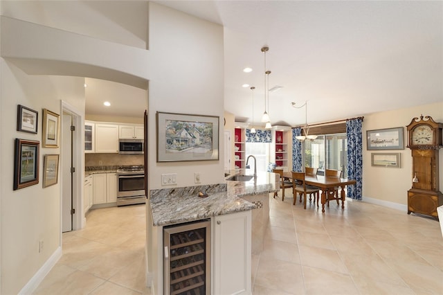 kitchen featuring wine cooler, arched walkways, stainless steel appliances, white cabinetry, and a sink