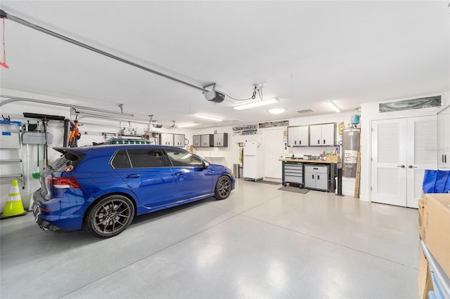 garage featuring gas water heater, freestanding refrigerator, and a garage door opener