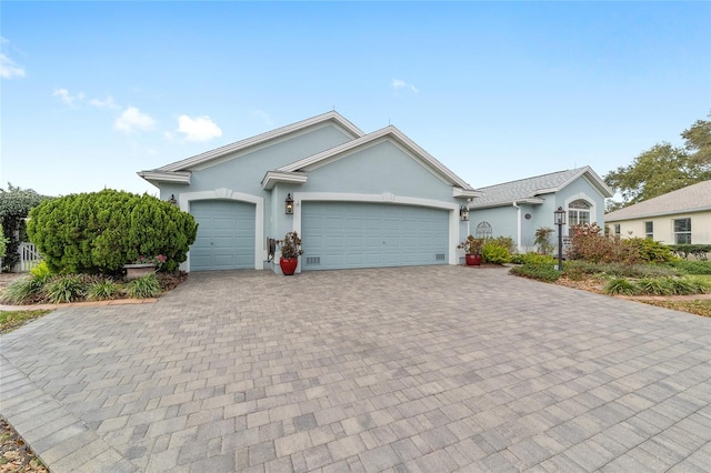 ranch-style house featuring an attached garage, decorative driveway, and stucco siding