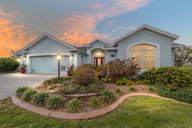 ranch-style house featuring a garage, decorative driveway, and stucco siding