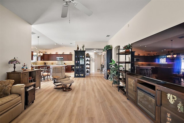 living room with light wood-style flooring, arched walkways, vaulted ceiling, and ceiling fan with notable chandelier