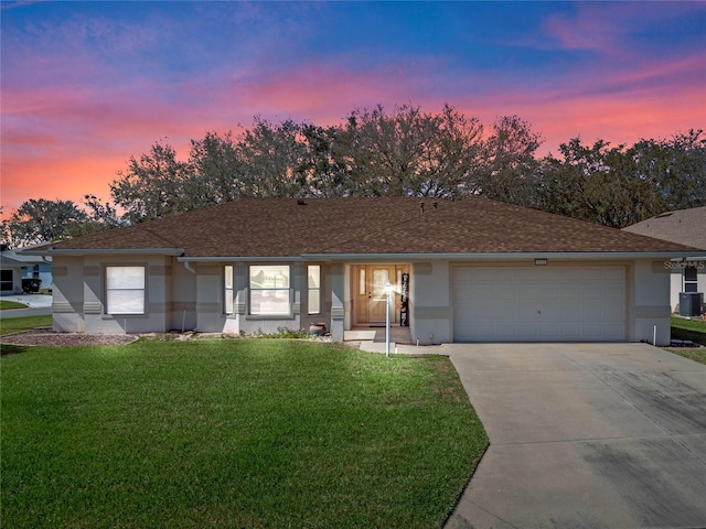 ranch-style house with a yard, stucco siding, central AC unit, a garage, and driveway