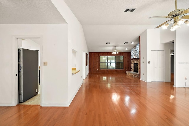 unfurnished living room with ceiling fan, a stone fireplace, vaulted ceiling, and light wood-style floors