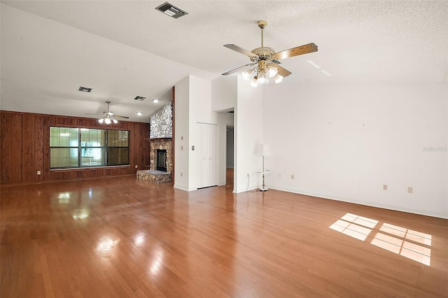 unfurnished living room with lofted ceiling, a textured ceiling, a stone fireplace, wood finished floors, and visible vents