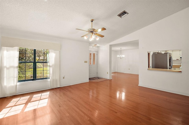 empty room featuring visible vents, wood finished floors, vaulted ceiling, a textured ceiling, and ceiling fan with notable chandelier