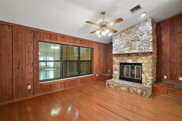 unfurnished living room with a stone fireplace, wood finished floors, visible vents, and wooden walls