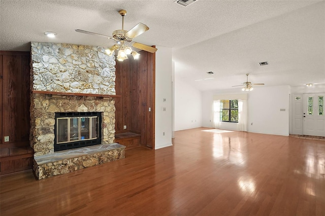 unfurnished living room featuring visible vents, ceiling fan, wood finished floors, a textured ceiling, and a stone fireplace