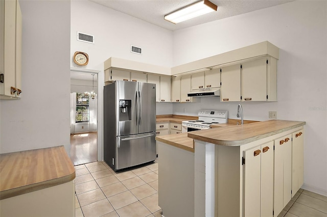 kitchen with white electric stove, under cabinet range hood, a peninsula, visible vents, and stainless steel refrigerator with ice dispenser