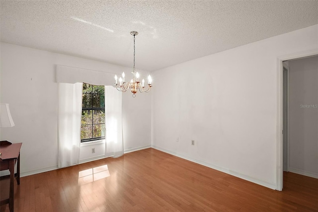 spare room with a textured ceiling, baseboards, wood finished floors, and an inviting chandelier