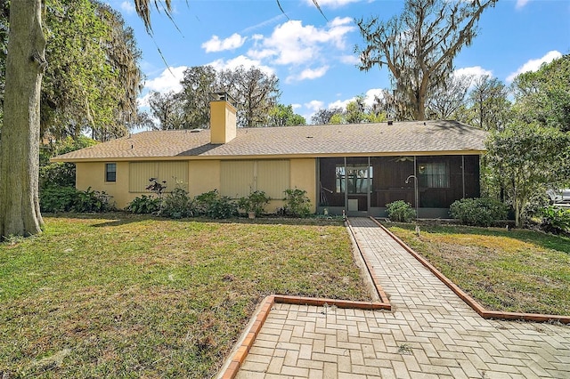 rear view of property featuring a sunroom, a chimney, and a lawn