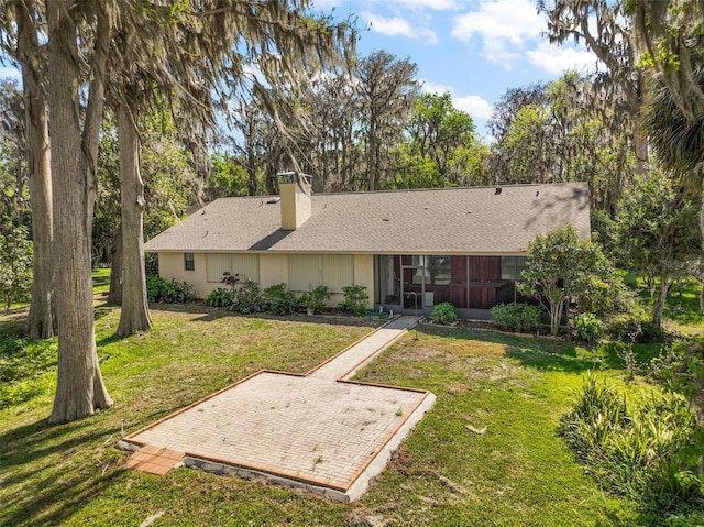 back of house with roof with shingles, a lawn, a chimney, and a sunroom