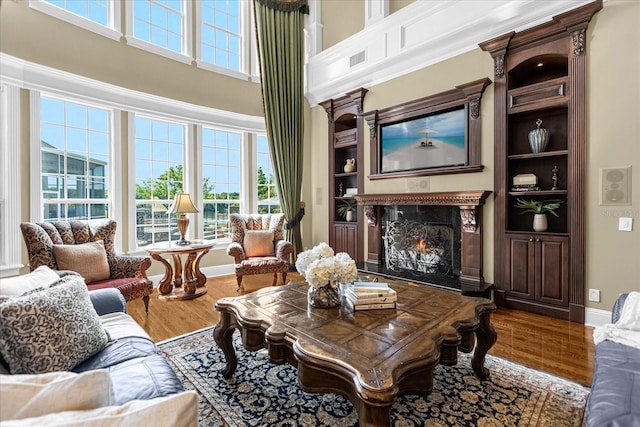 living area featuring a high ceiling, a fireplace, wood finished floors, built in features, and baseboards