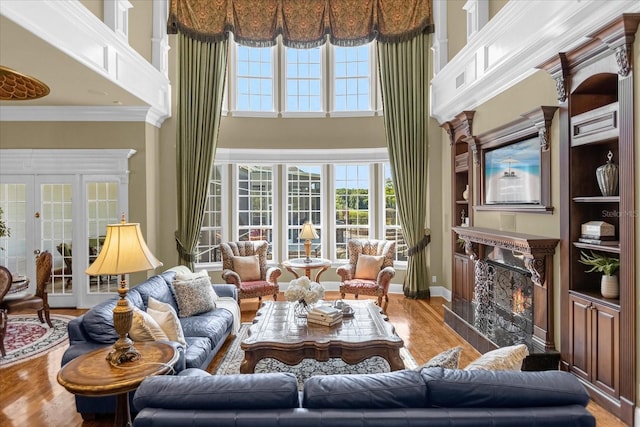 living room with a towering ceiling, wood finished floors, crown molding, french doors, and a high end fireplace