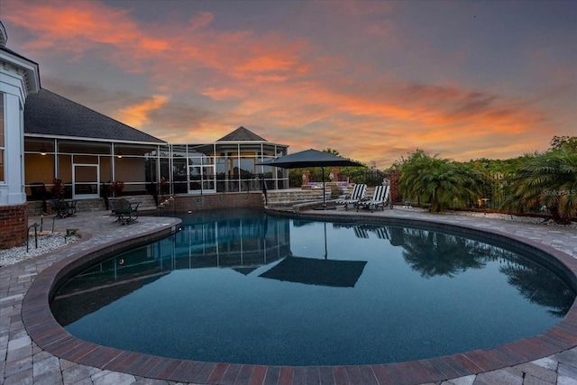 pool at dusk with an outdoor pool and a patio